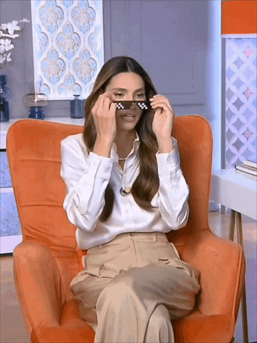 a woman is sitting in an orange chair and wearing sunglasses