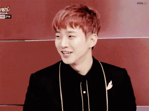 a young man with red hair is smiling in front of a red wall with 2pm written on it