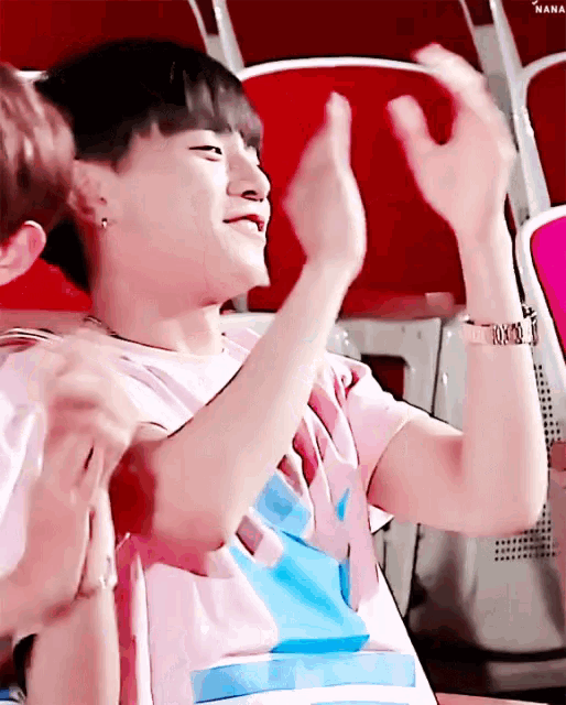 a man in a pink shirt is sitting in a chair with his hands in the air .