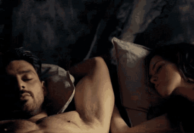 a man without a shirt is laying next to a woman who is sleeping