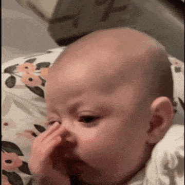 a baby is laying on a floral pillow and touching its nose .