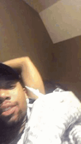 a man wearing a hat is laying on a bed with his hand on his head .