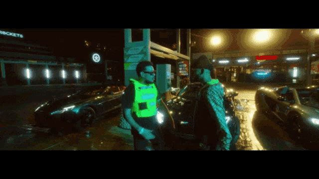 a man in a yellow vest stands next to another man in a green vest