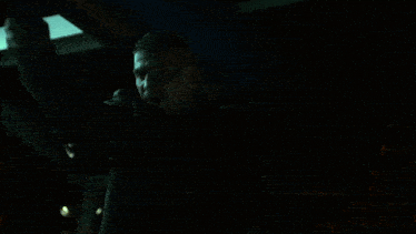 a person in a black shirt is standing in the dark looking out a window at night .