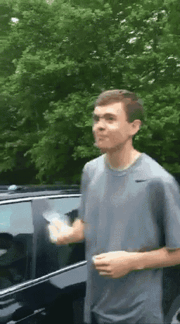 a man in a gray shirt is standing in front of a car