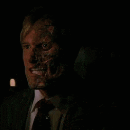 a man in a suit and tie with a scary face is looking at the camera .