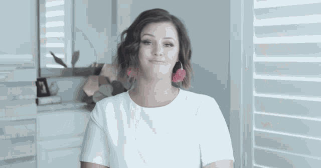 a woman wearing a white shirt and pink earrings smiles