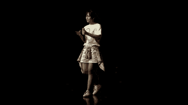 a young girl in a white shirt and shorts is standing in the dark with her hands on her hips .