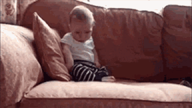 a baby is sitting on a couch with two pillows on it