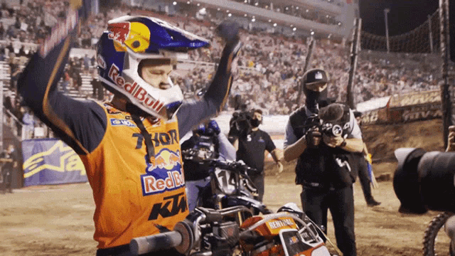 a man wearing a red bull helmet stands in front of a motorcycle