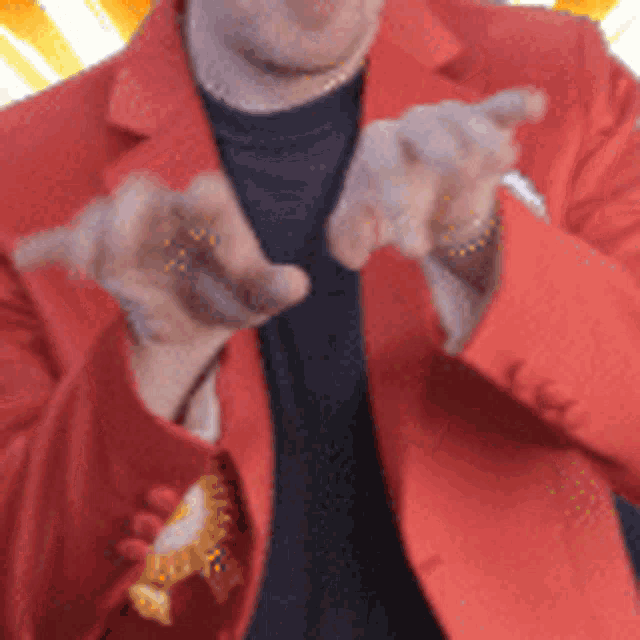 a man in a red jacket and black shirt is pointing at the camera