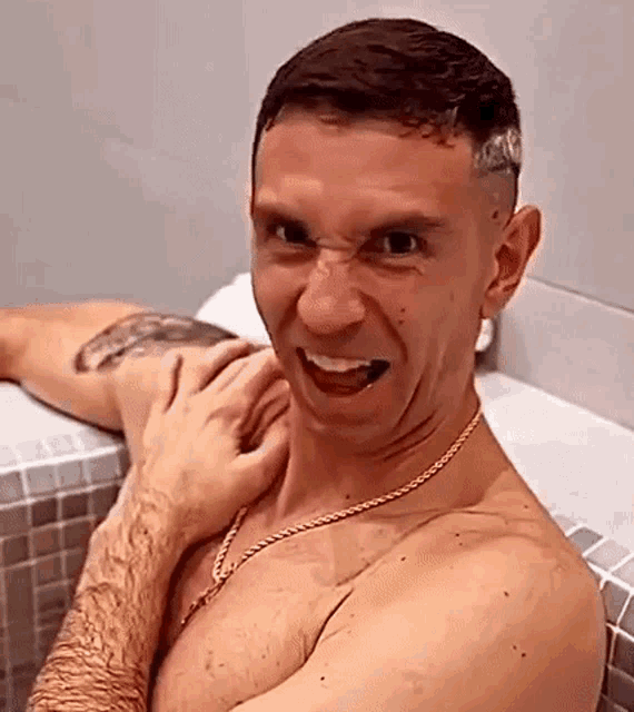 a shirtless man is sitting in a bathtub making a funny face while a woman holds his arm .