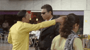 a man in a yellow shirt is talking to a man in a black jacket