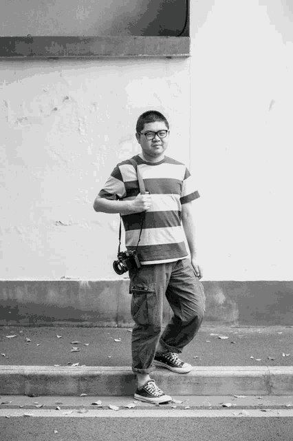 a man in a striped shirt is holding a camera and giving the thumbs up
