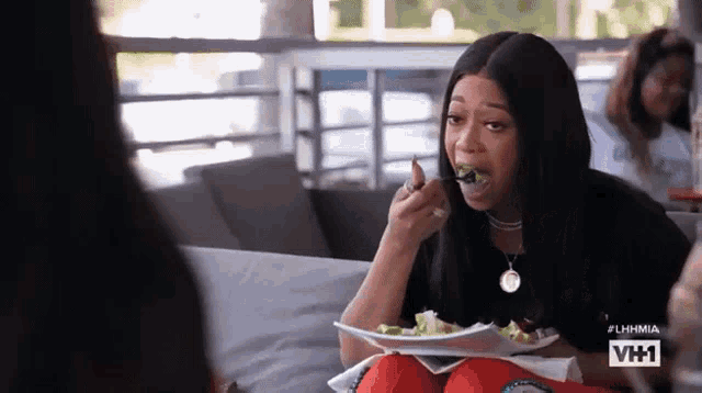 a woman is sitting on a couch eating a salad .