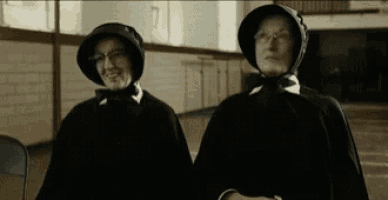 two women are standing next to each other in a room wearing black robes and hats .