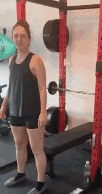 a woman is standing in a gym next to a bench and barbell .