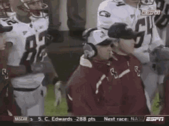 a group of football players standing around a coach wearing headphones .