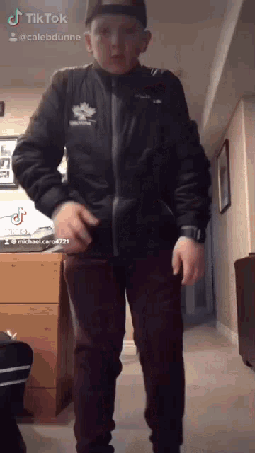 a boy wearing a black jacket with a maple leaf on it is standing in a hallway