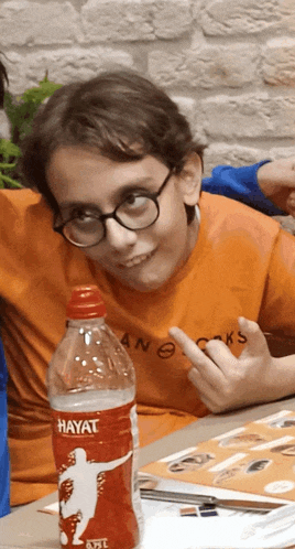 a boy wearing glasses is sitting at a table next to a hayat bottle