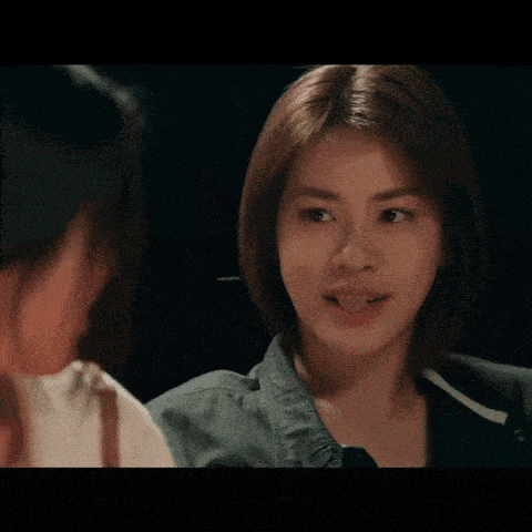 a woman with short hair is looking at another woman in a dark room