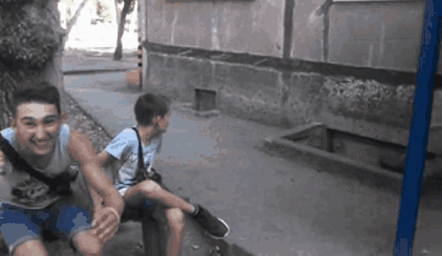 two young men are sitting on a sidewalk laughing and smiling