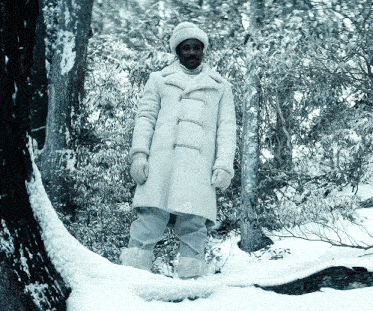 a man in a white coat is standing in the snow near a tree