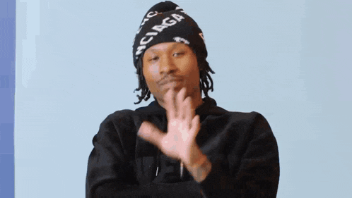a man wearing a balenciaga hat and a black hoodie is making a peace sign .
