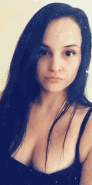 a woman with long black hair is wearing a black tank top with a plunging neckline .