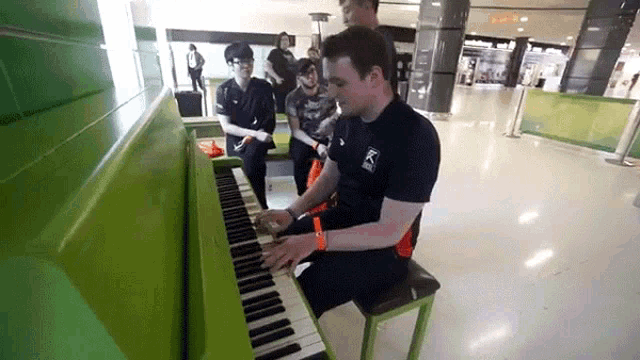 a man is playing a green piano while a group of people watch
