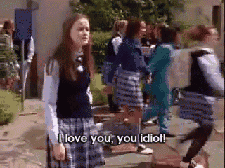 a girl in a school uniform is standing in front of a crowd of people and says i love you , you idiot .