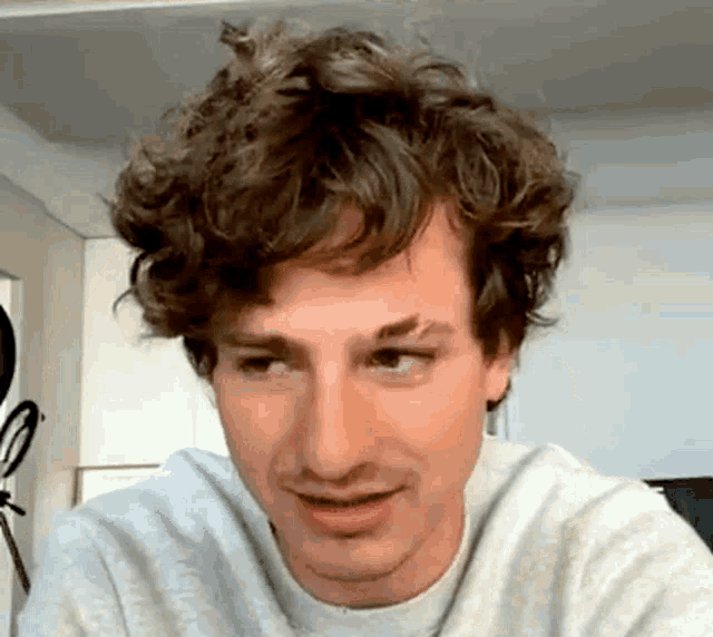 a man with curly hair is smiling and wearing a gray sweater .
