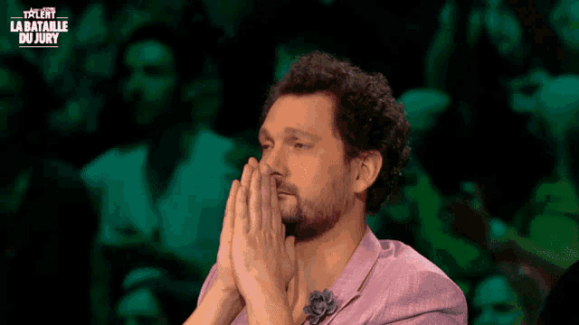 a man with his hands folded in front of a screen that says talent la bataille du jury