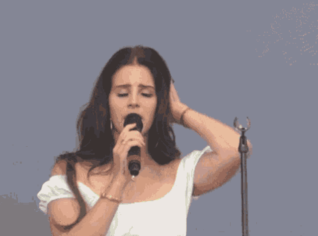 a woman is singing into a microphone while holding her hair