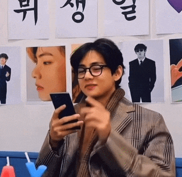 a young man wearing glasses is holding a cell phone