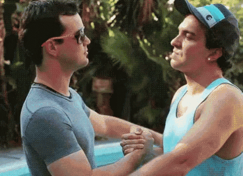 two men are shaking hands in front of a pool while wearing sunglasses and hats .
