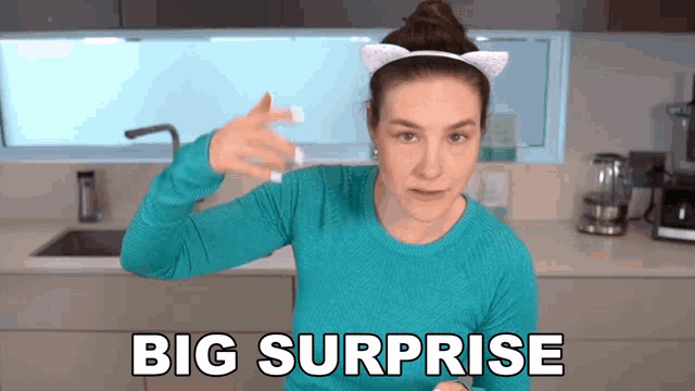 a woman wearing cat ears and a blue sweater says big surprise