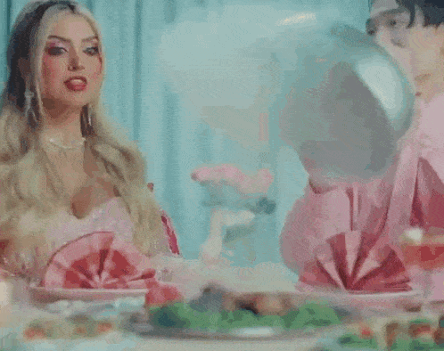 a woman in a pink dress is sitting at a table with plates of food and a man in a pink shirt .