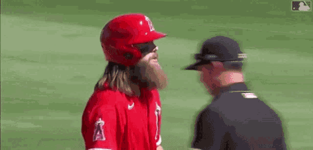 a baseball player with a beard is talking to a referee on a field .