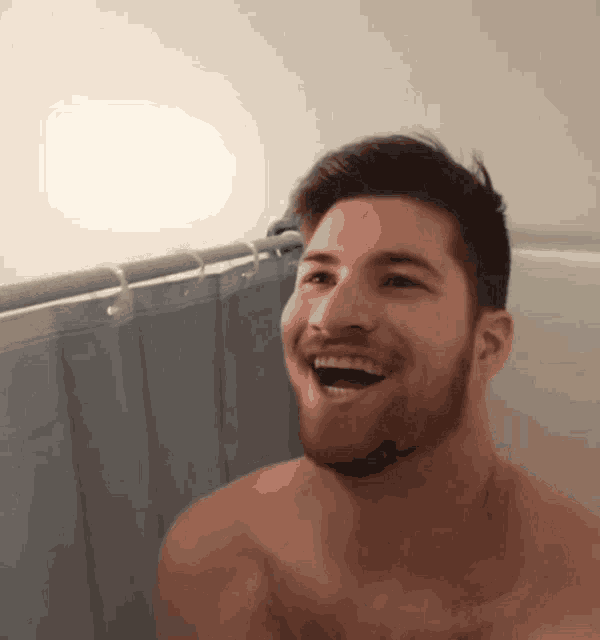 a shirtless man with a beard is laughing in a shower