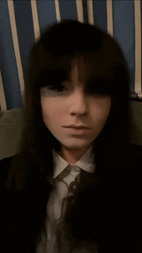 a woman with long dark hair is sitting on a couch with a person 's hand on her head