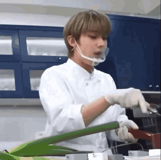 a man wearing a mask and gloves is cutting vegetables in a kitchen .