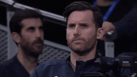 a man with a beard is sitting in a stadium watching a game with a camera in front of him .