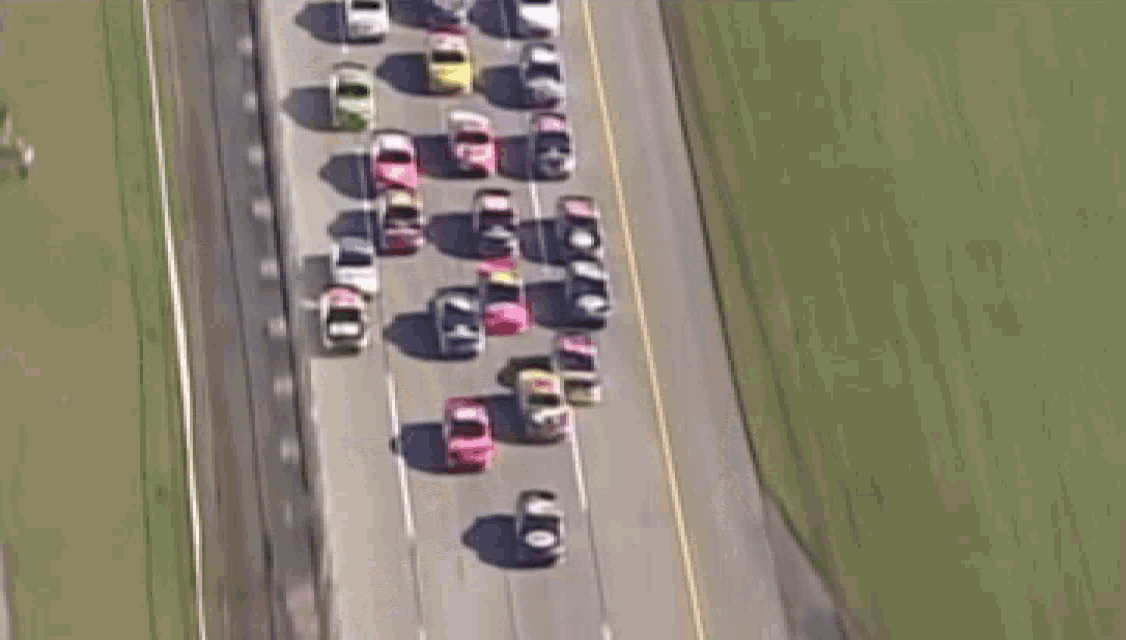 a bunch of cars are driving down a road with their shadows on the ground