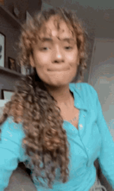 a woman with curly hair wearing a blue shirt is making a funny face .