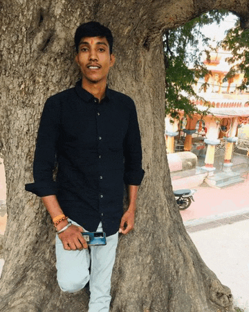 a young man leaning against a tree with a phone in his hand
