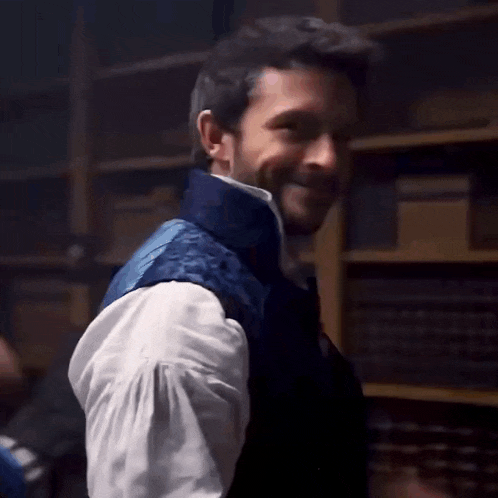 a man in a white shirt and blue vest is making a funny face