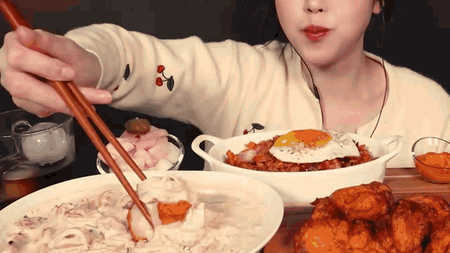 a woman is eating food with chopsticks while wearing a sweater with a cherry on it