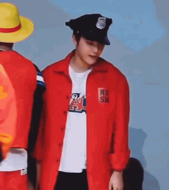 a man in a red jacket and a police hat is standing next to another man in a yellow hat .