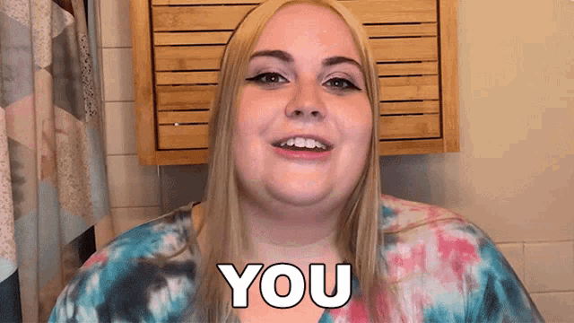 a woman in a tie dye shirt is smiling and saying you